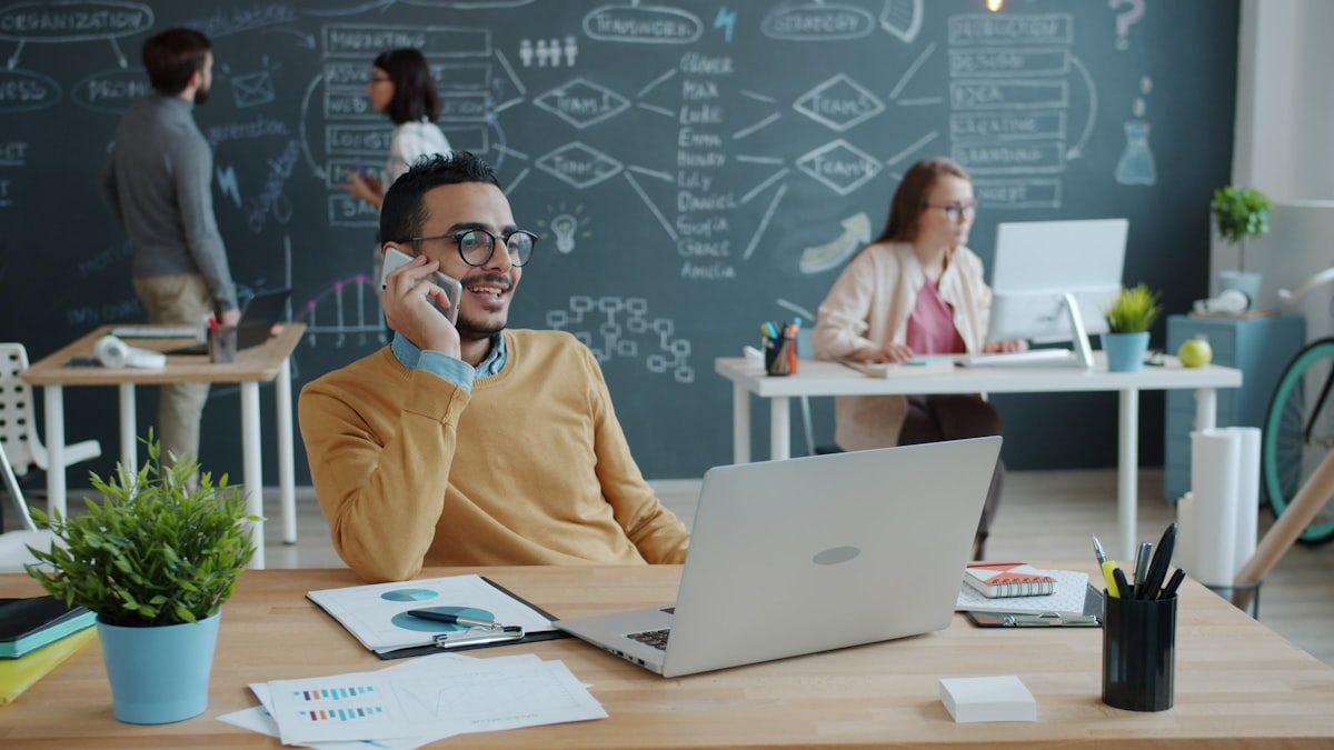 Agent commercial au téléphone à son bureau, collègues travaillant en arrière-plan