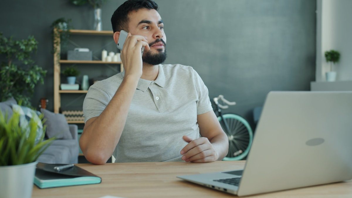 Homme au téléphone à son domicile devant un ordinateur portable sur le bureau